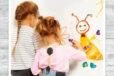 Zwei Kinder malen mit Buntstiften an eine Wand.